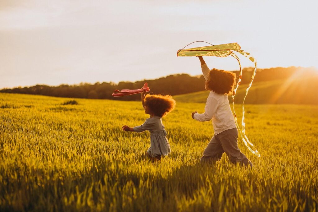 Brother-sister-playing-with-kite-plane-field-sunset